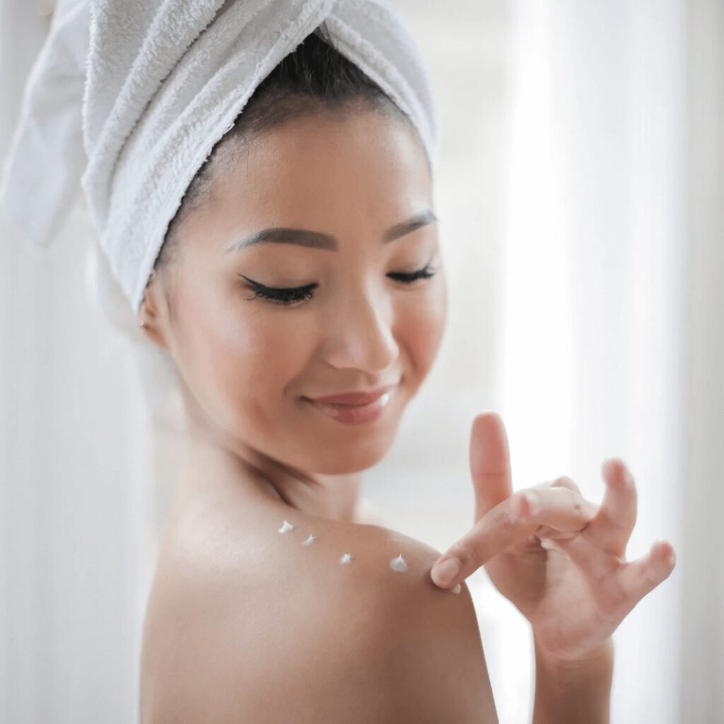 asian girl putting lotion on her shoulder