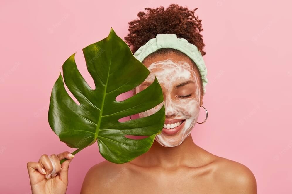 brown girl with cleansing face and green leaf in the left hand with light background