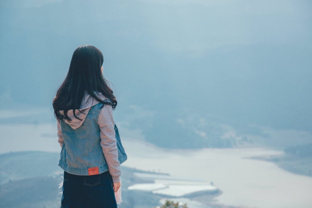 woman in gray and blue zip up hoodie standing on the cliff trying to move on