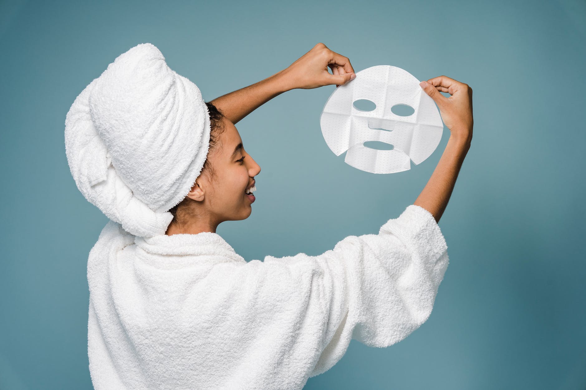 cheerful young black lady showing sheet mask and smiling after bath